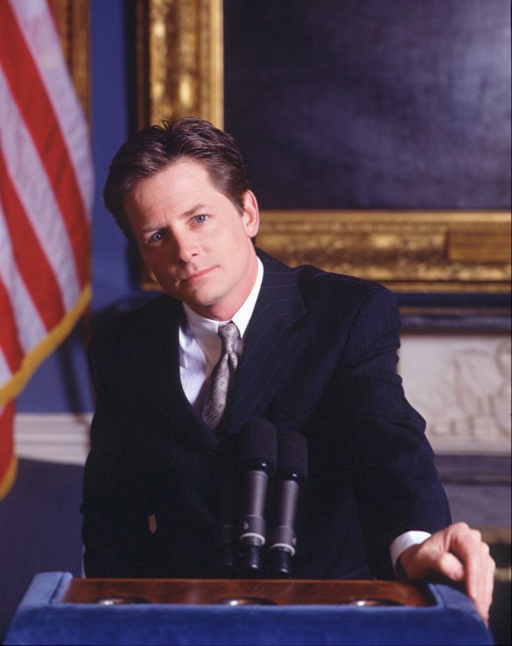 a man wearing a suit and tie standing at a podium in front of an american flag