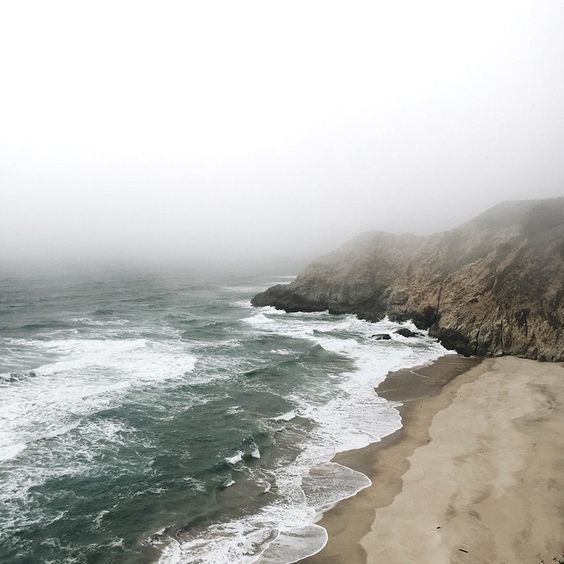 an ocean view with waves crashing on the shore and fog in the sky above it