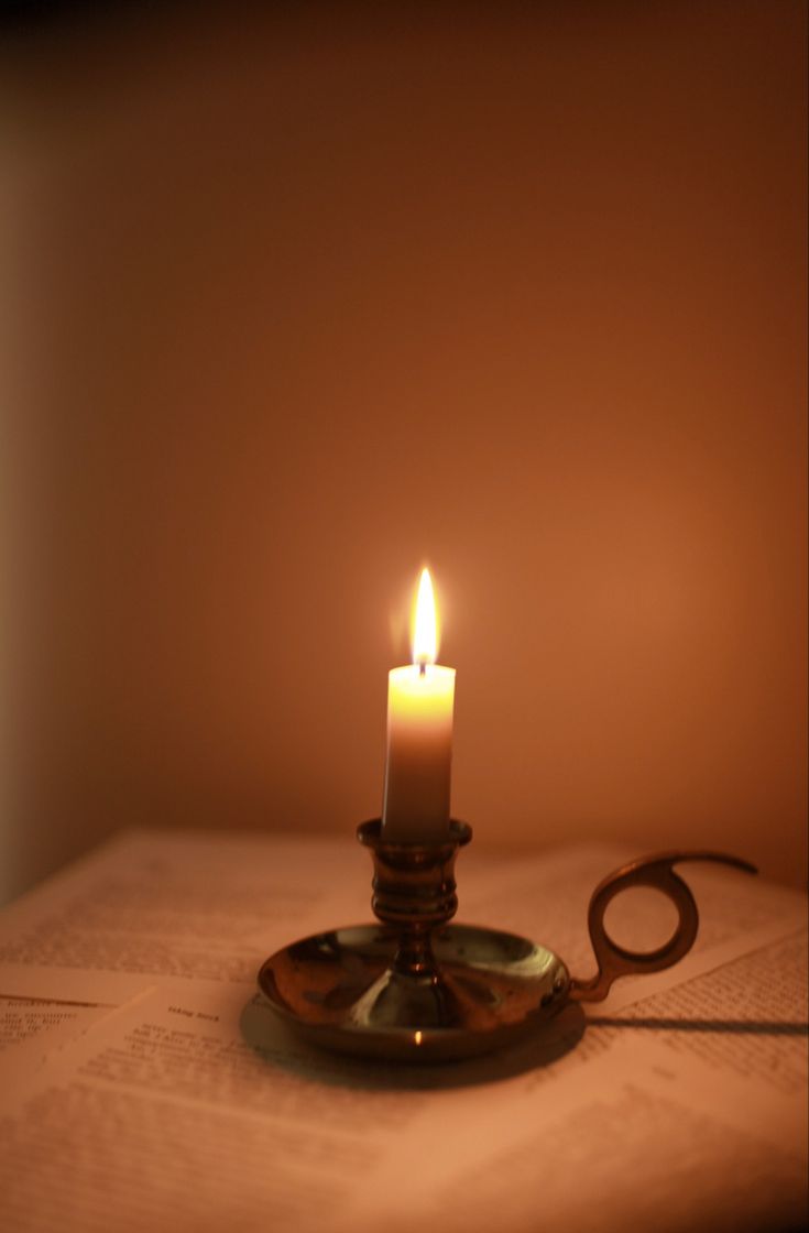 a lit candle sitting on top of an open book next to a pair of scissors