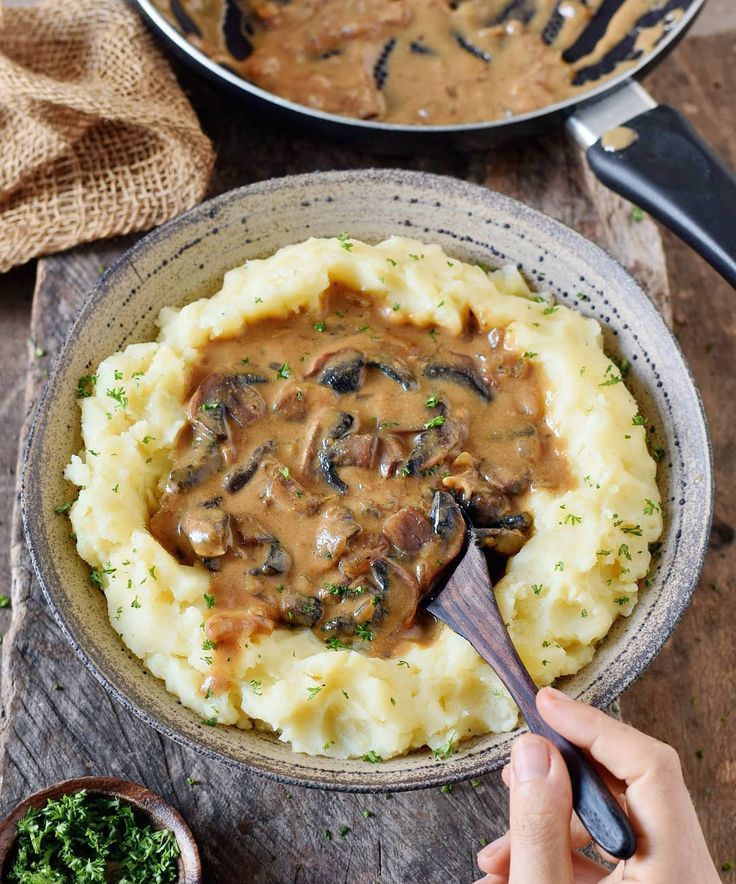 someone is spooning mashed potatoes with mushroom gravy in a bowl on a wooden table