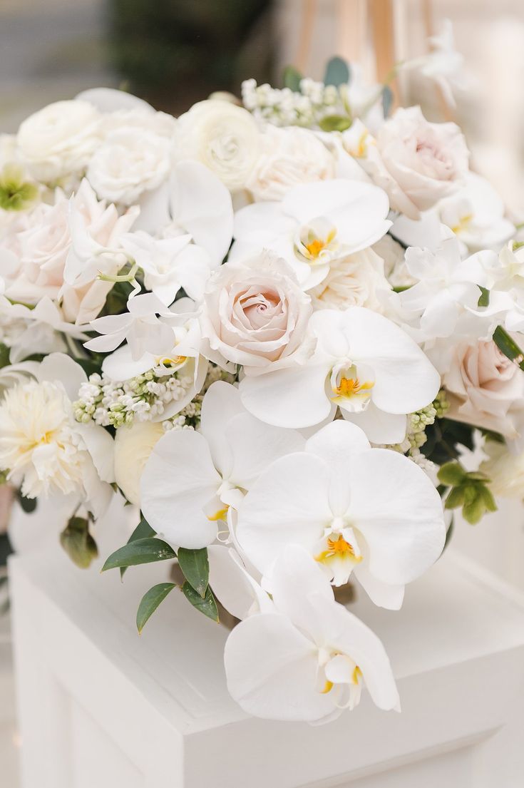 a bouquet of white and pink flowers sitting on top of a white box with greenery