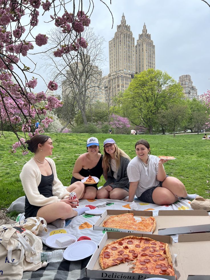 three women sitting on the grass eating pizza