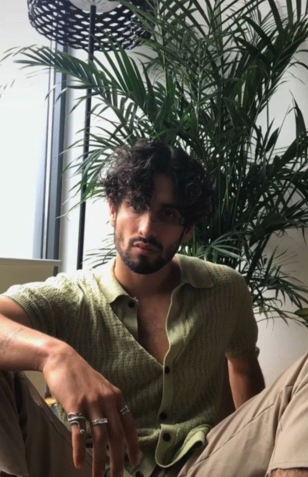 a man sitting on the floor next to a potted plant and wearing a green shirt