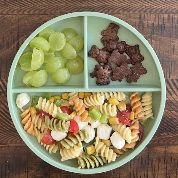 a green bowl filled with pasta and veggies on top of a wooden table