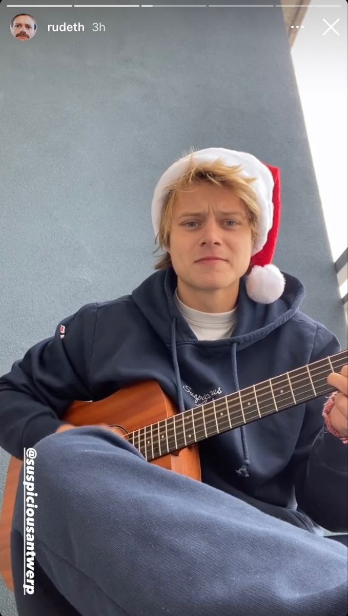 a young man wearing a santa hat while playing an acoustic guitar