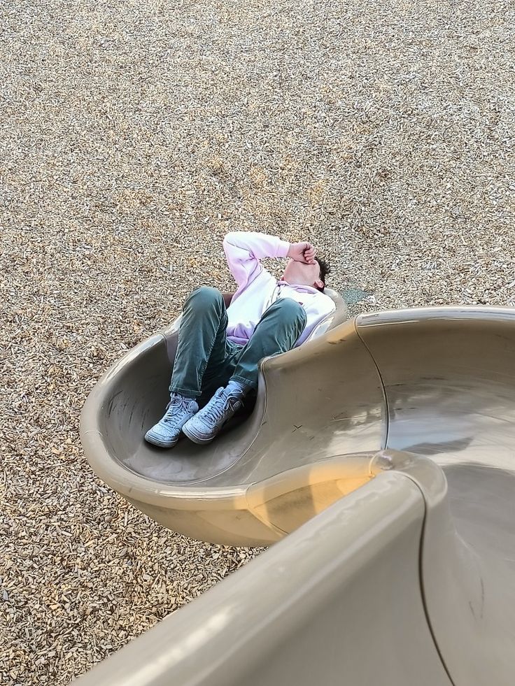 a man laying on top of a slide in the middle of a gravel covered field