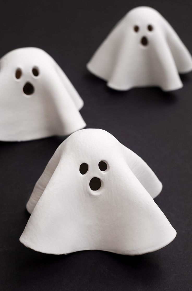 three white ghost - like objects with black eyes and nose are on a dark surface