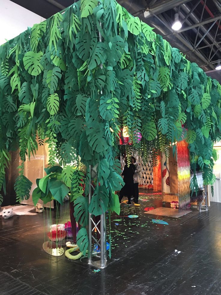 a room filled with lots of green plants on the walls and floor, while people are walking around