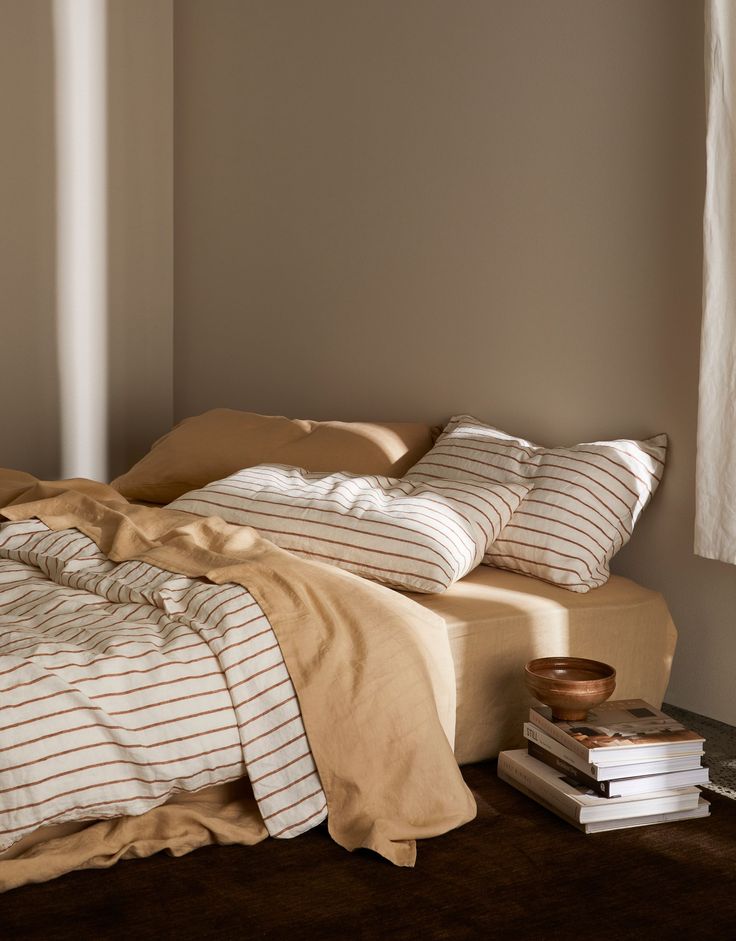 a bed sitting next to a window with white curtains and pillows on top of it