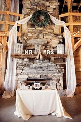 a table with a white cloth on it in front of a stone fireplace and wooden beams