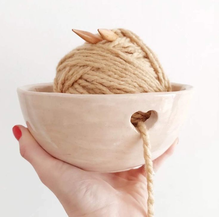 a ball of yarn in a bowl being held by a woman's hand