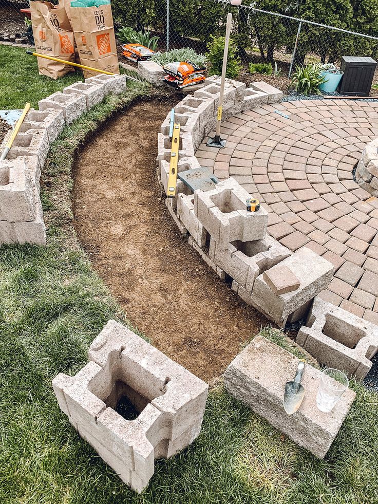 a brick fire pit in the middle of a yard with bricks around it and tools on the ground