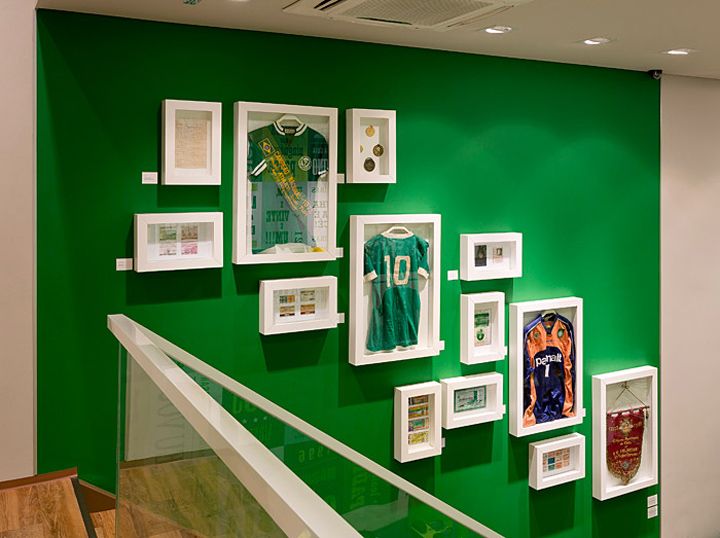 a green wall with white frames and pictures hanging on it's side as well as framed sports memorabilia