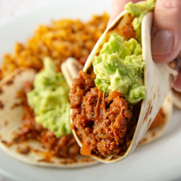 a person is holding a tortilla filled with meat and guacamole