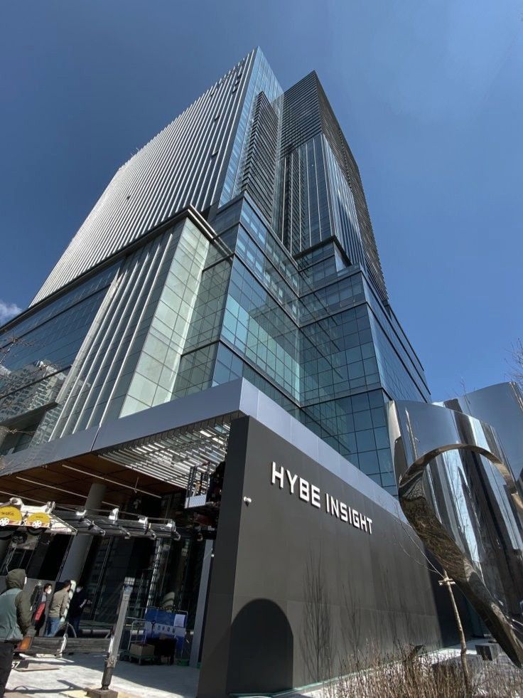 people are walking around in front of a large building with glass and steel on it