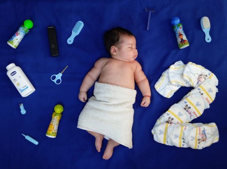 a baby laying on top of a blue blanket next to items that include toothbrushes