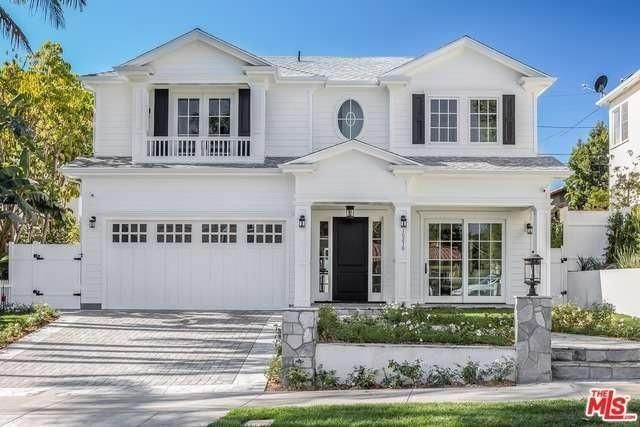 a white house with black shutters on the front and side windows, surrounded by palm trees