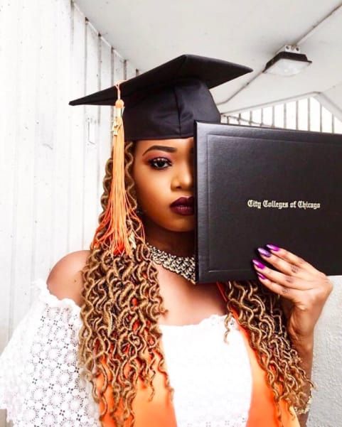 a woman with long hair wearing a graduation cap and gown holding up a book in front of her face