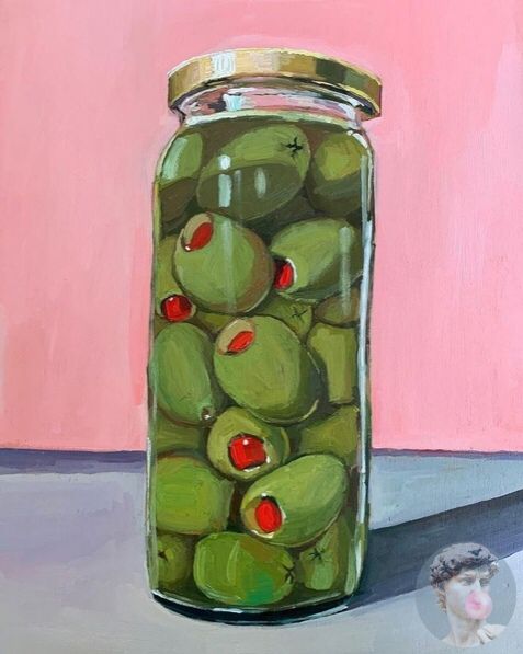 a jar filled with green olives on top of a table next to a pink wall