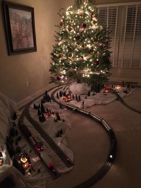 a christmas tree is lit up in the corner of a room with toy train tracks