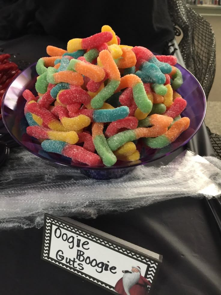 a bowl filled with gummy bears on top of a table next to a sign