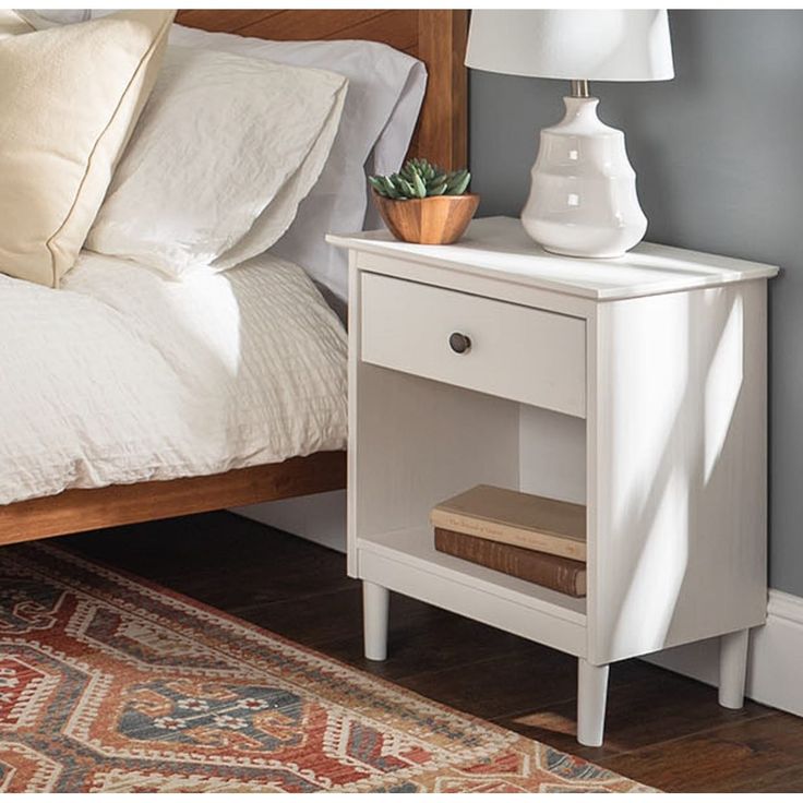 a white nightstand with a plant on it next to a bed