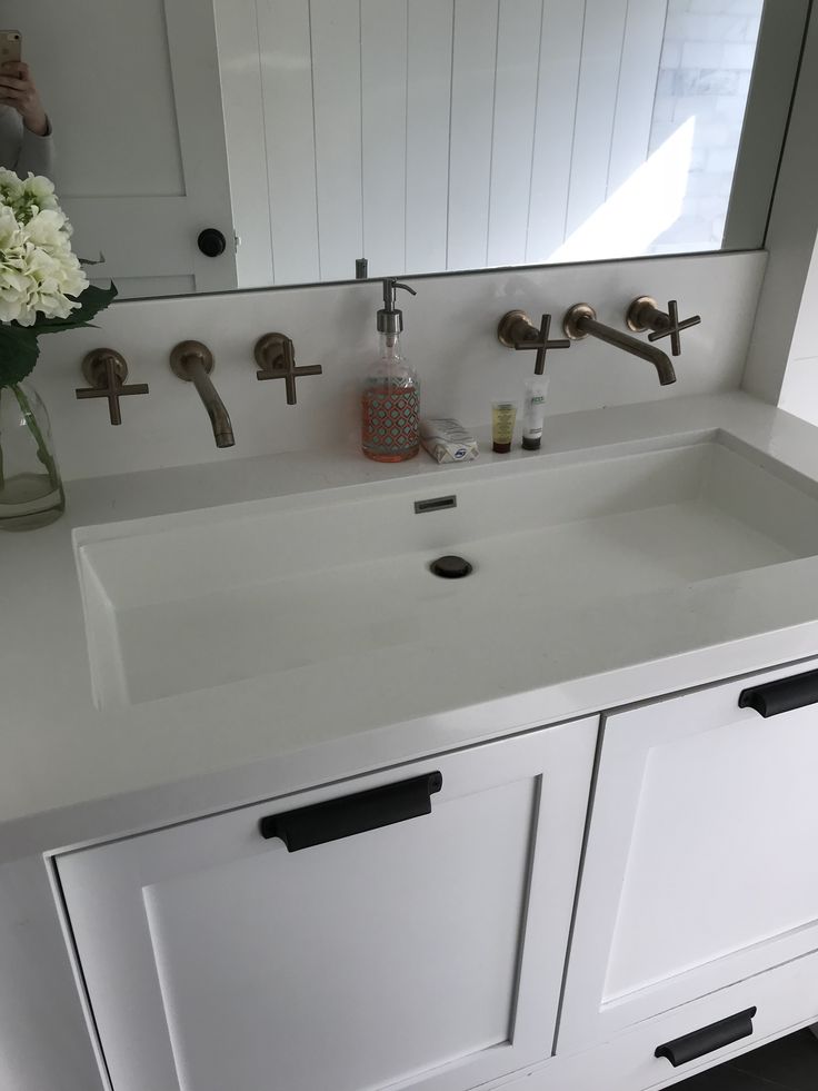 a white bathroom sink sitting under a mirror next to a vase with flowers in it