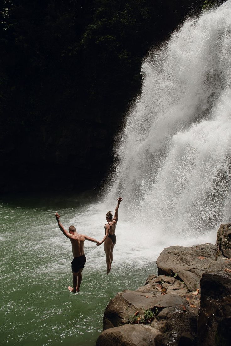 two people jumping off the side of a waterfall