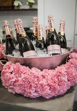 a metal bowl filled with champagne bottles on top of a table next to pink flowers