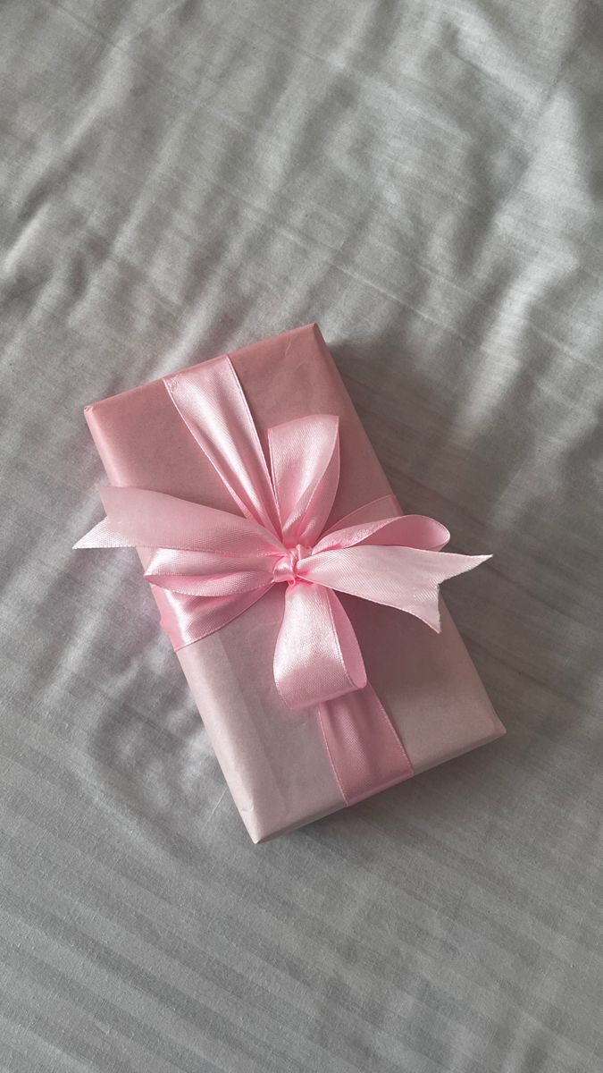 a pink gift box wrapped in satin ribbon on top of a gray bed sheet with white sheets