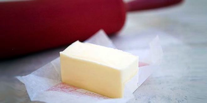 a piece of butter sitting on top of wax paper next to a red container and knife