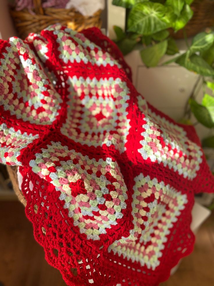 a red and white crocheted blanket sitting on top of a wooden table next to a potted plant