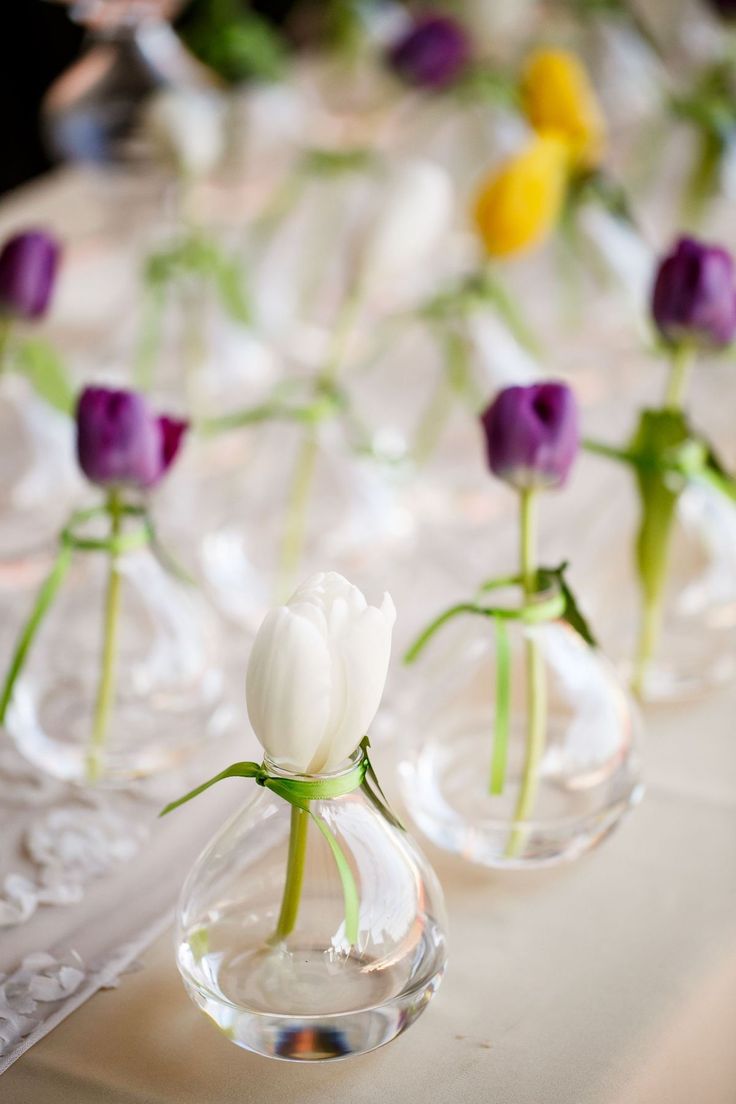 small vases with flowers in them sitting on a white table cloth covered tablecloth