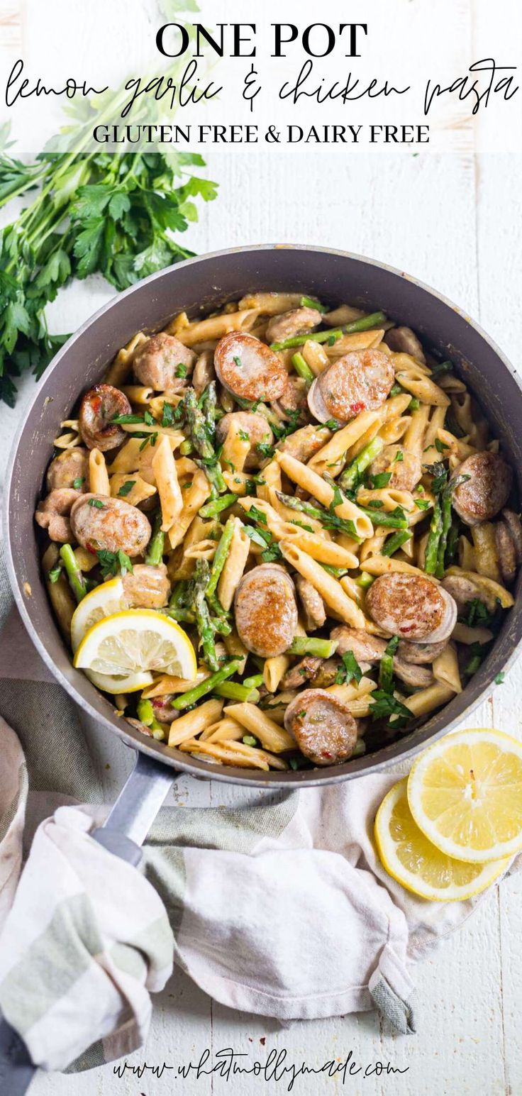 a skillet filled with pasta, asparagus and meatballs next to lemon wedges