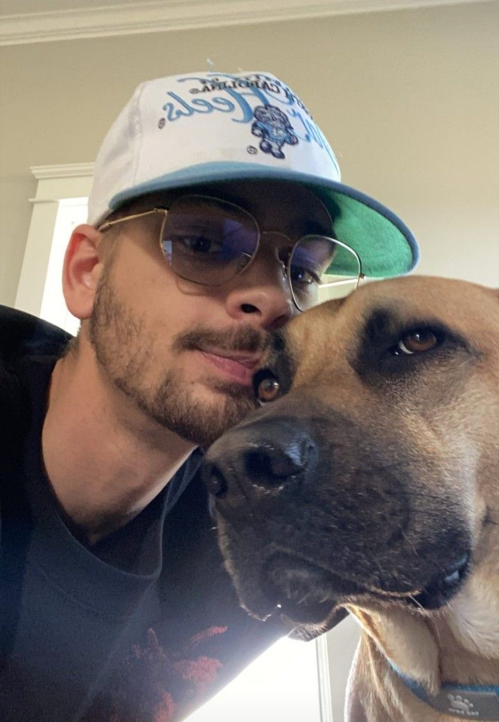 a man wearing glasses and a hat is hugging his dog's face in front of the camera