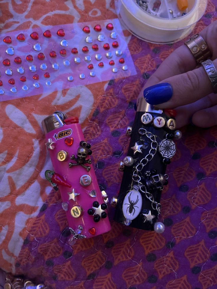 a person is holding two cell phones with chains and charms on them, one has blue nail polish and the other has gold