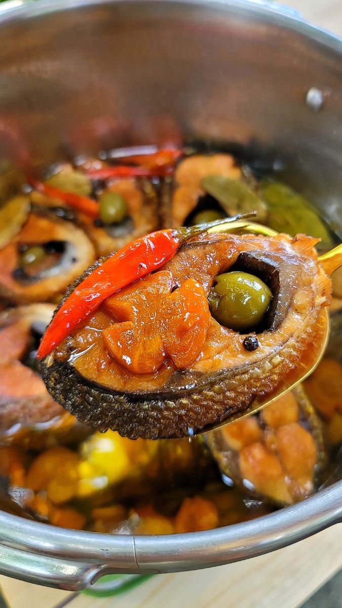 a spoon with some food in it on top of a pot filled with vegetables and sauce