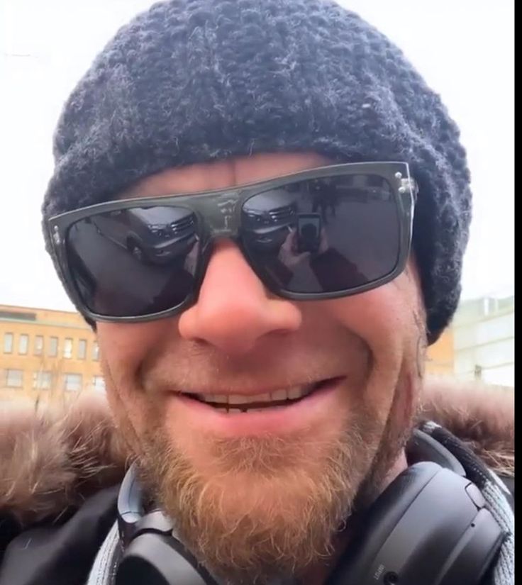 a man wearing sunglasses and a hat with headphones on his ears is smiling at the camera