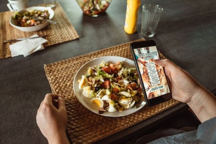 a person holding a cell phone over a plate of food