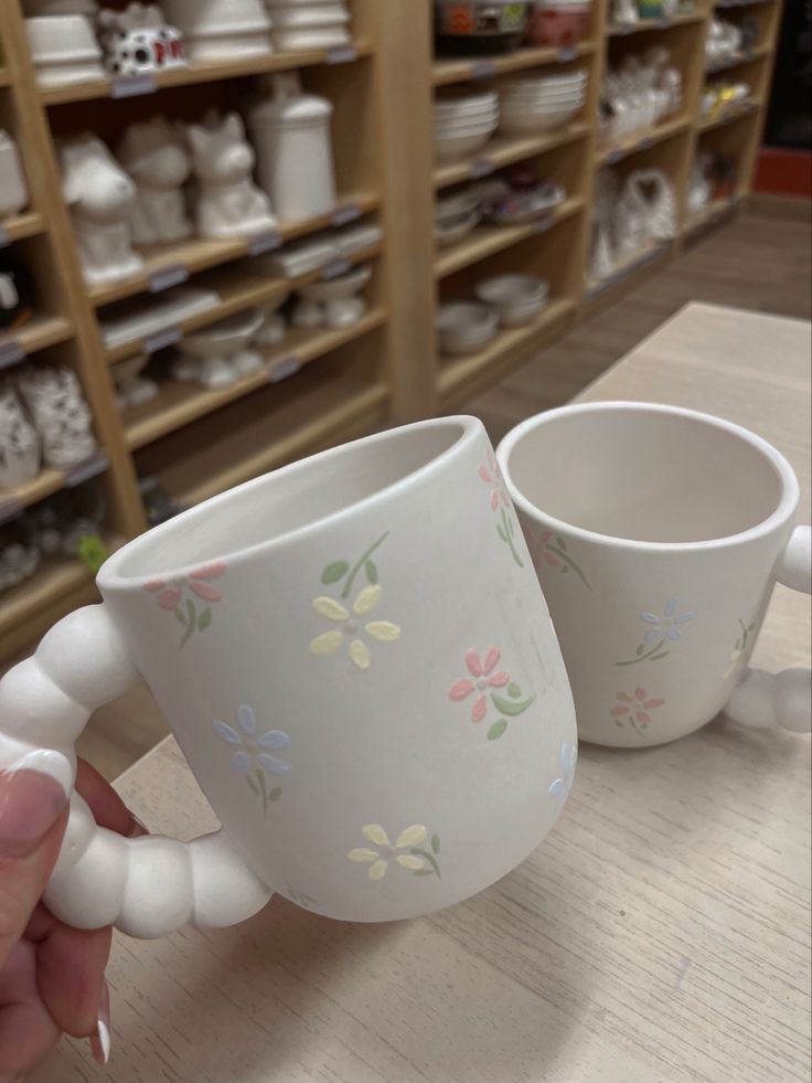 two coffee mugs sitting on top of a wooden table next to shelves filled with dishes