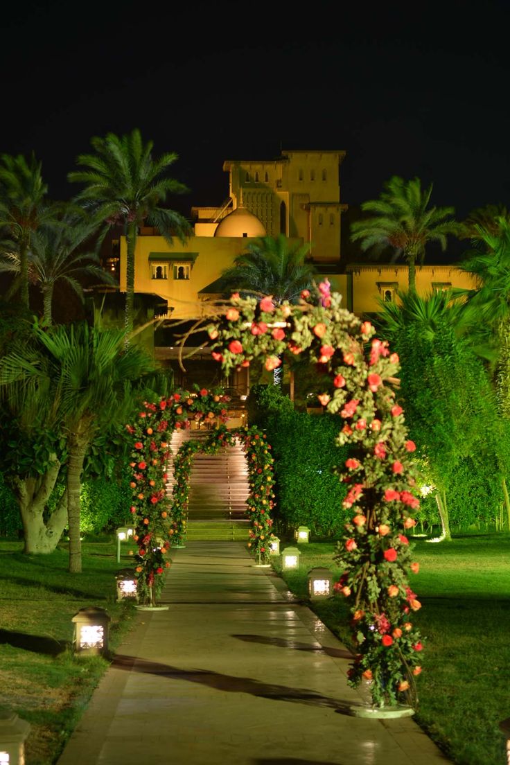 an outdoor walkway decorated with flowers and lit candles at night in front of a large building