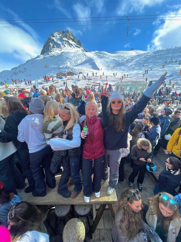 a group of people standing on top of a snow covered slope next to a mountain