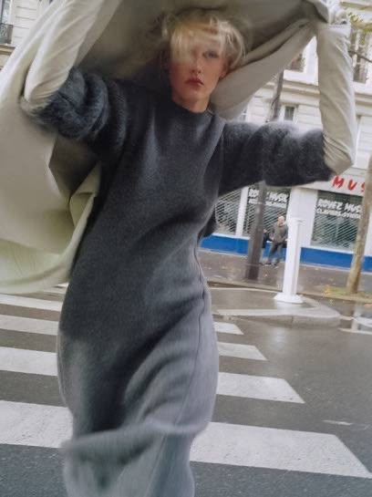 a woman is walking down the street with an umbrella over her head and she's wearing a gray dress