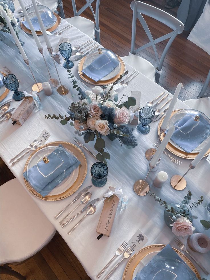 the table is set with blue and white plates, silverware, and floral centerpieces