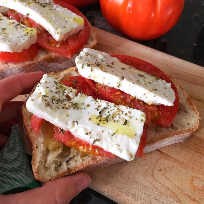 someone is holding their sandwich with tomatoes and cheese on it as they prepare to eat