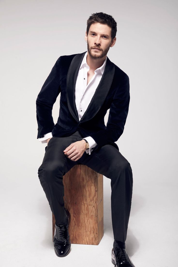 a man sitting on top of a wooden block wearing a suit and tie with his hands in his pockets