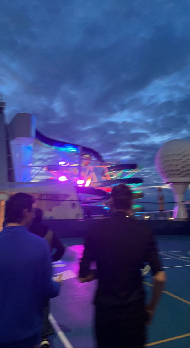 two people standing on a tennis court at night with the sky lit up behind them