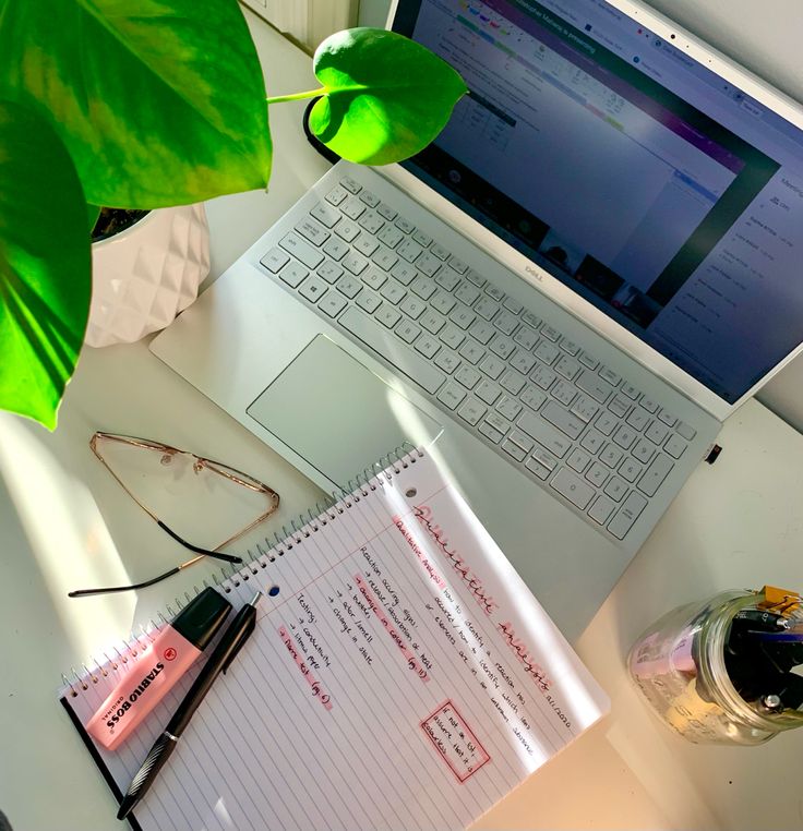 an open laptop computer sitting on top of a white desk next to a green plant