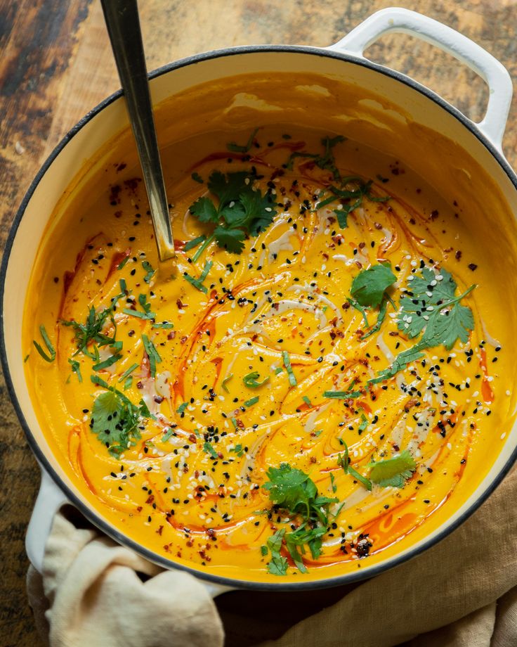 a bowl of soup with carrots and parsley in it on a wooden table