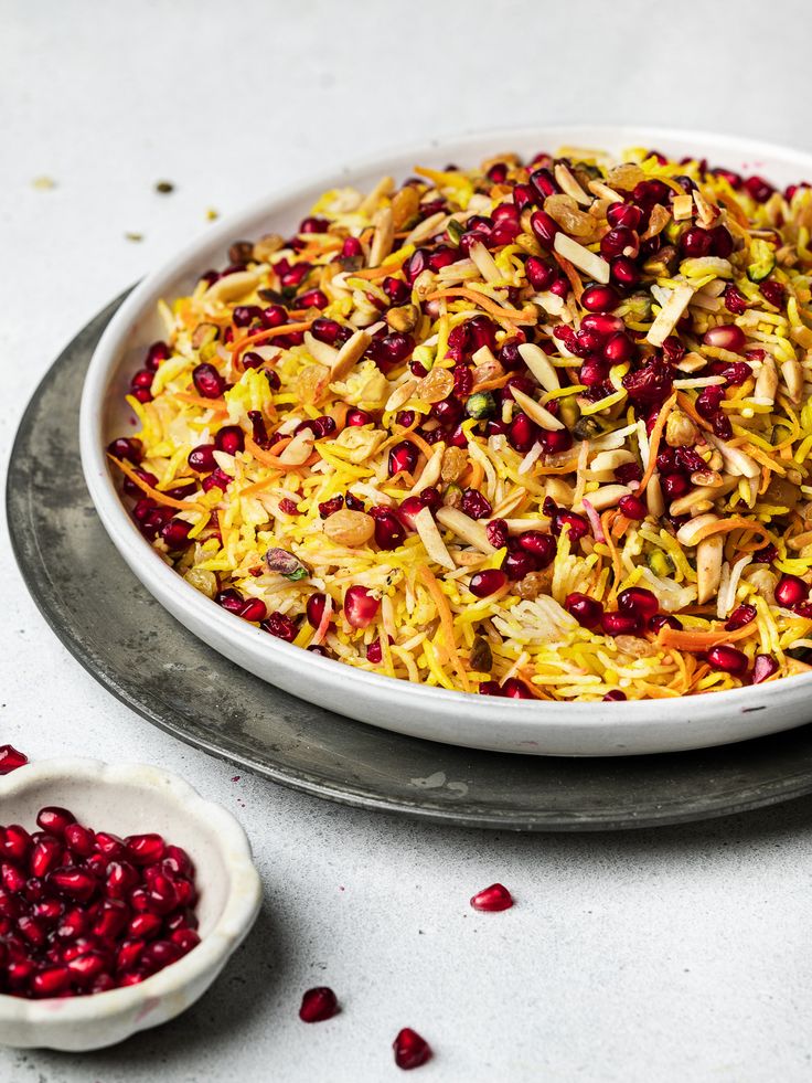 a white bowl filled with cranberries and nuts next to a small bowl of pomegranates